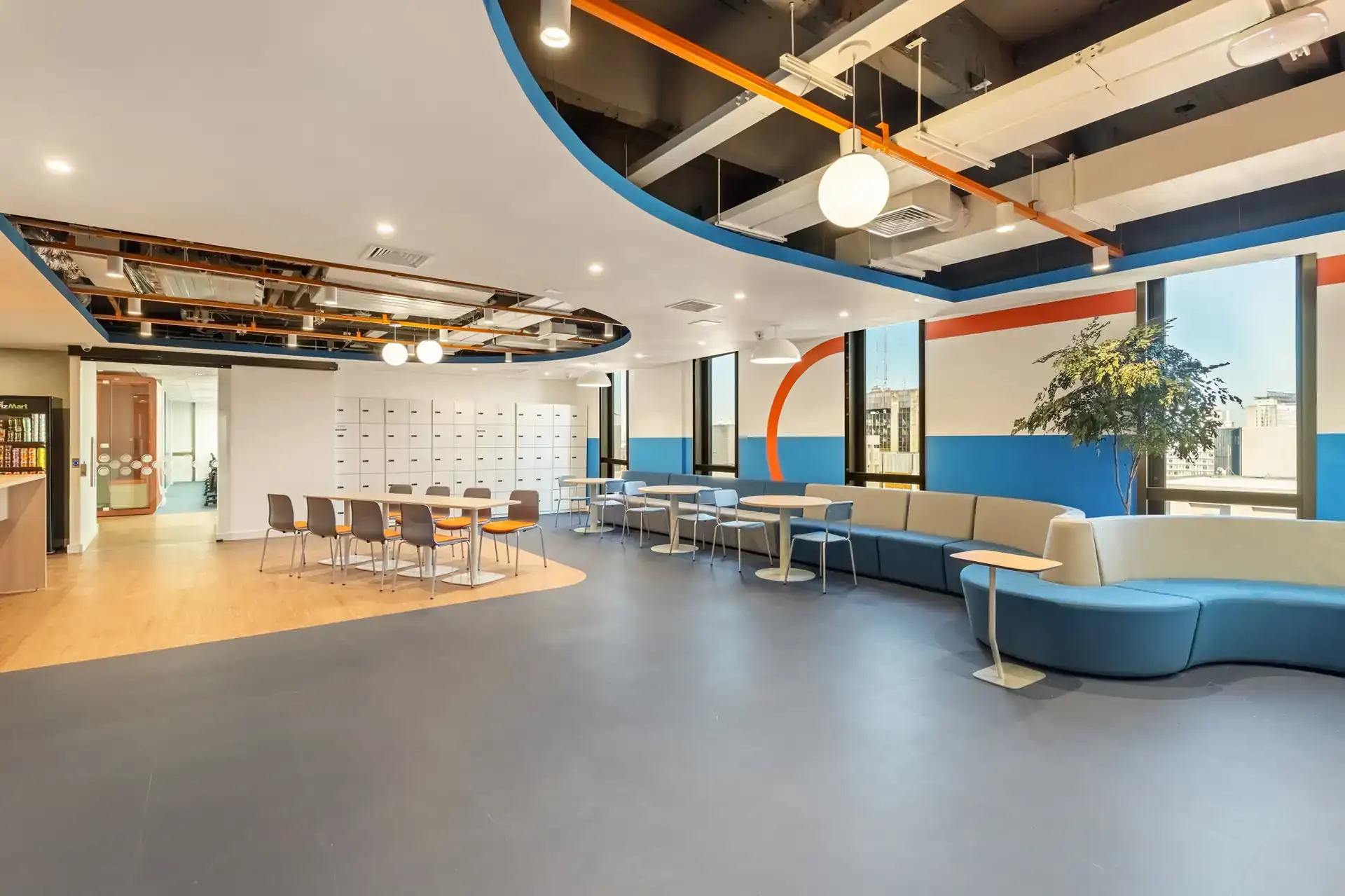 Área de convivência ampla com mesas, lockers e cores vibrantes, parte de um projeto de arquitetura para o escritório da Recovey, em São Paulo, focado em bem-estar da equipe.