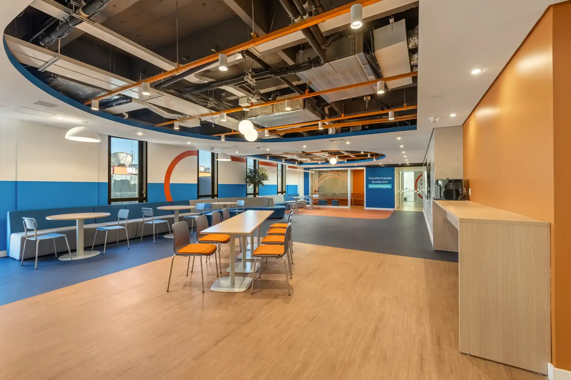 Espaço social colorido com mesas coletivas e cadeiras modernas, exemplificando design corporativo descontraído e funcional. Pensado em reforma corporativa com projeto de arquitetura e obra para o escritório da Recovery.