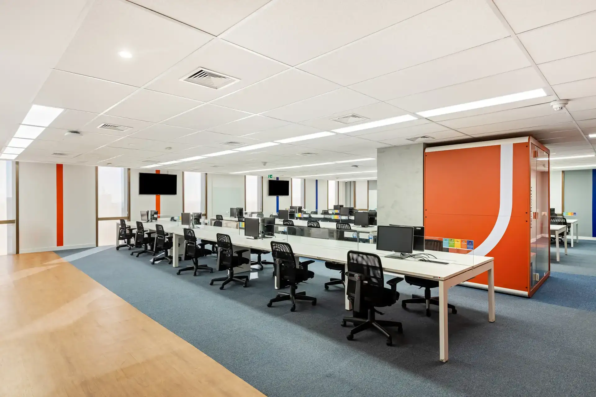 Área aberta com estações de trabalho iluminadas, mostrando um projeto de arquitetura corporativa com foco em funcionalidade e amplitude, no escritório da Recovery.