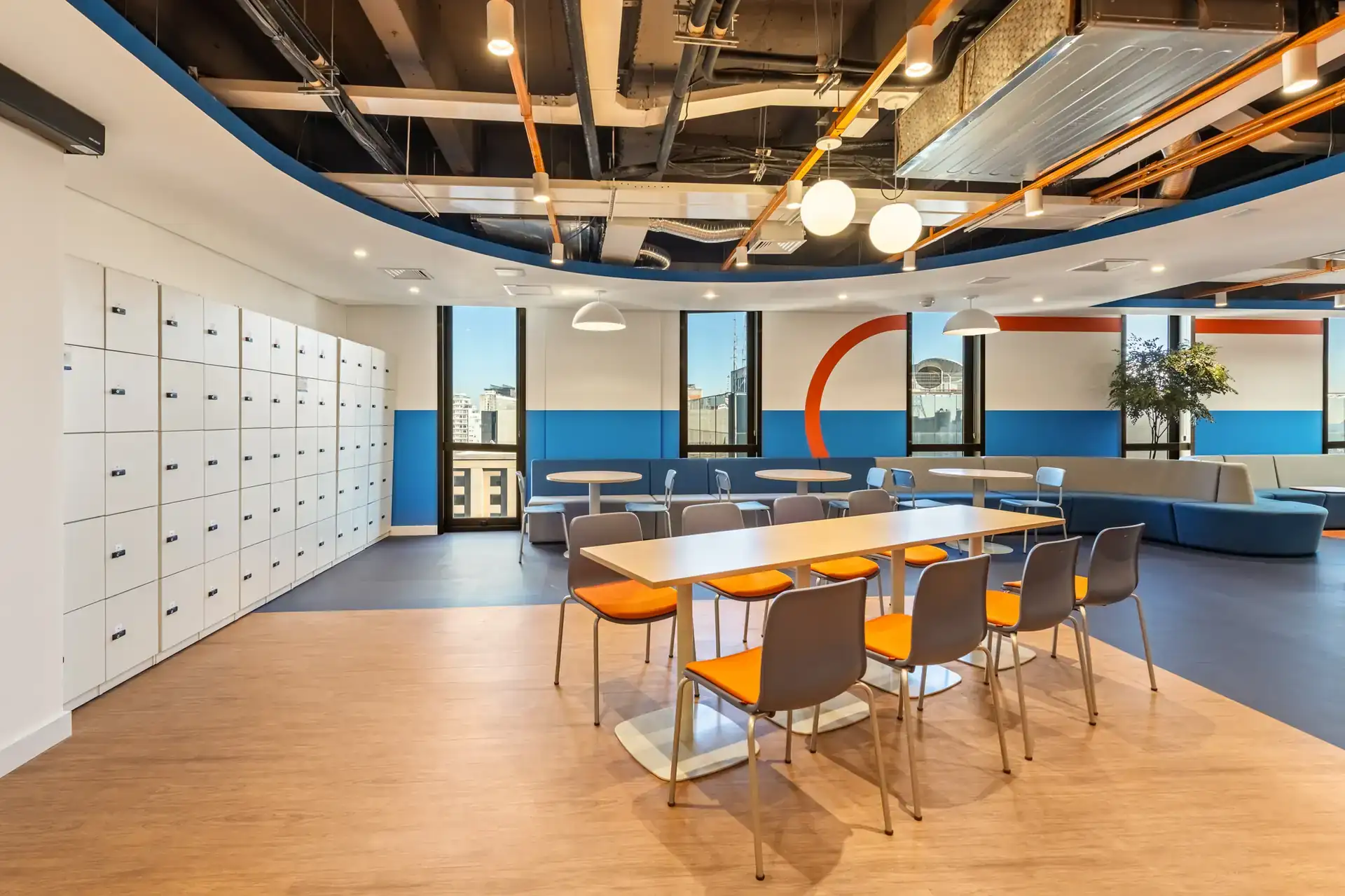 Lockers brancos e mesas coletivas em salão amplo, parte de um projeto de arquitetura corporativa para o escritório da Recovery que prioriza fluxo e organização.