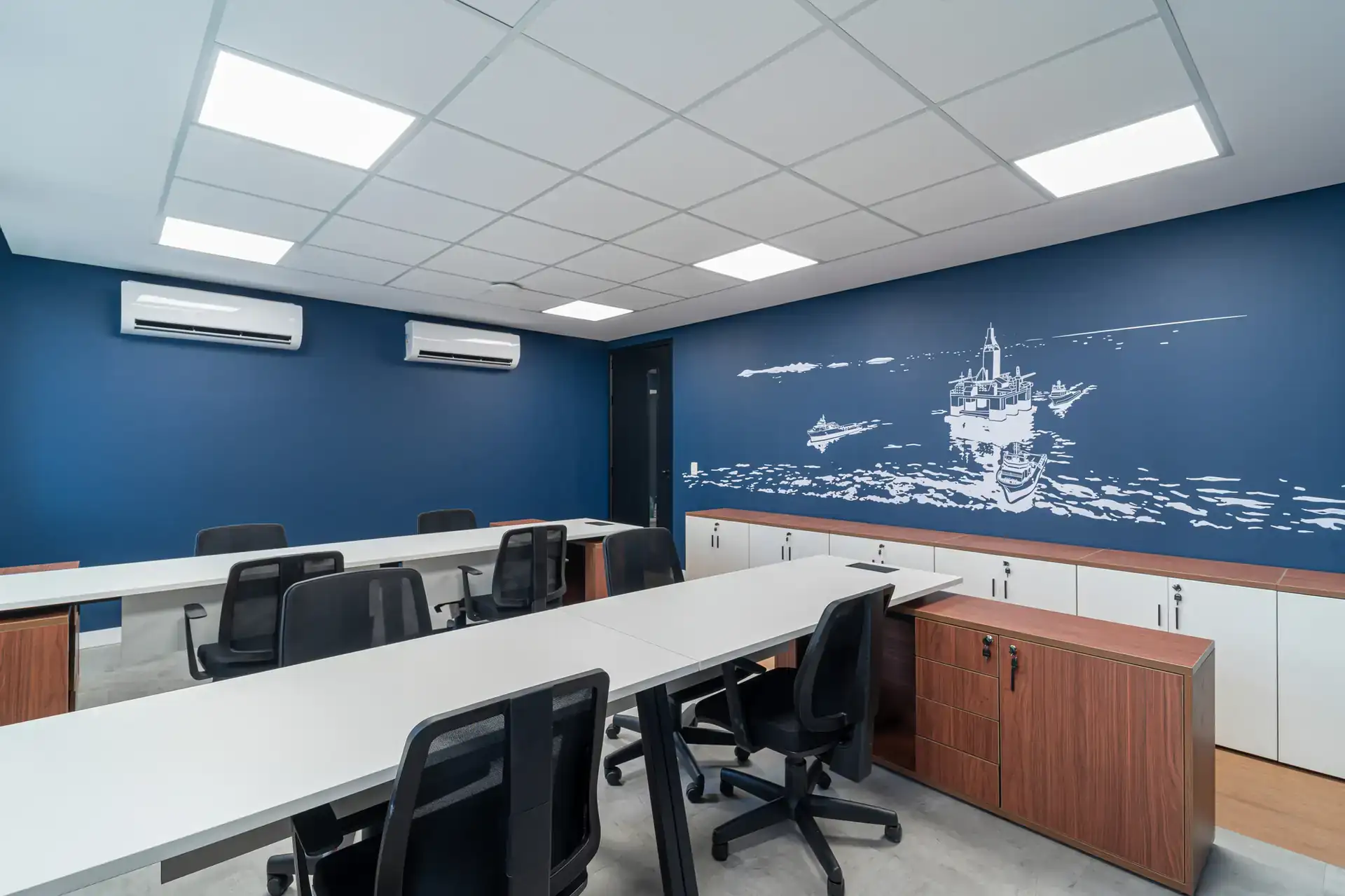 Sala de atendimento com mural marítimo em parede azul e mobiliário leve, criada em projeto de arquitetura feito em reforma corporativa.