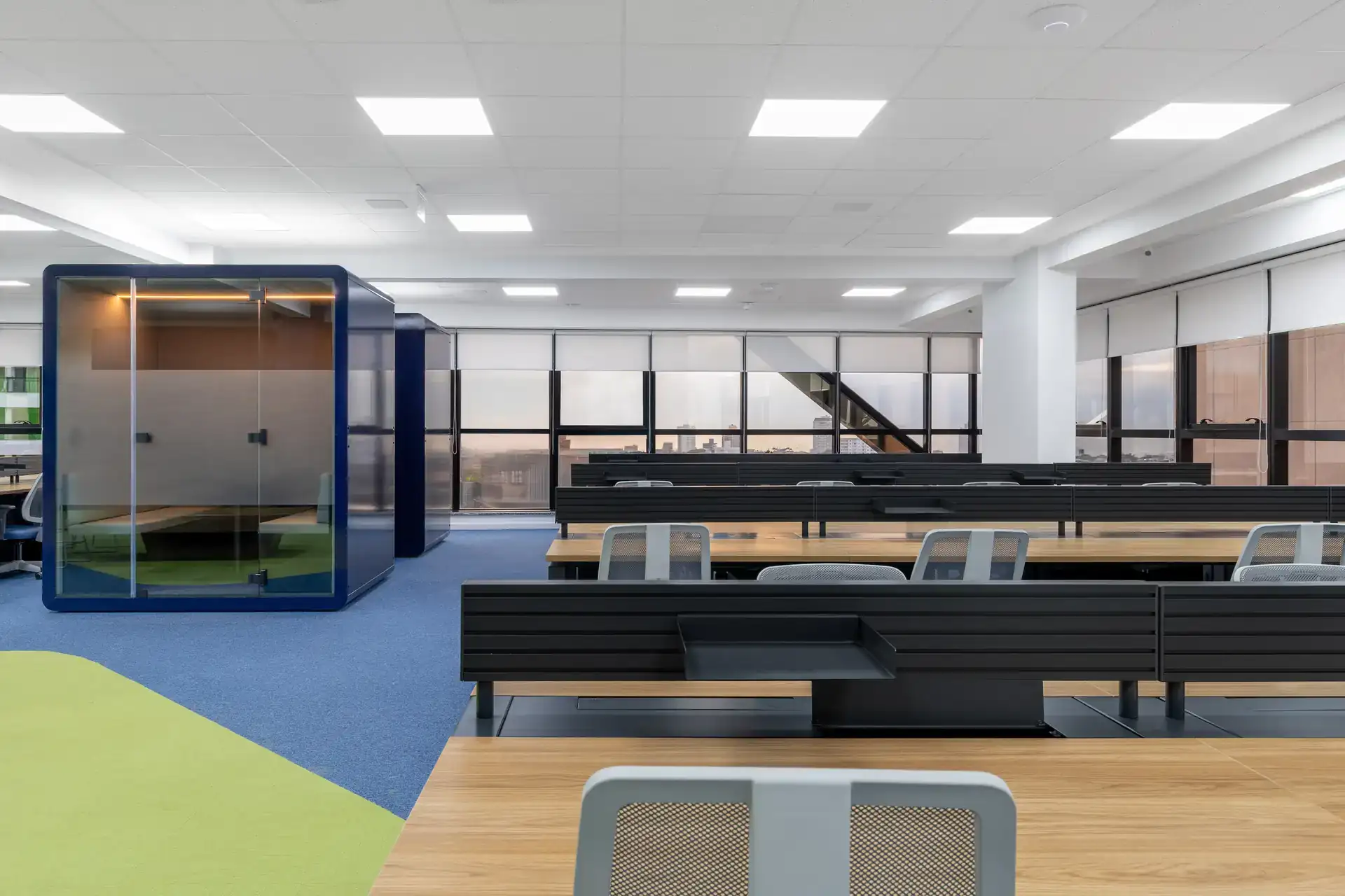 Estações de trabalho amplas em open space após reforma de escritório corporativo, destacando marcenaria integrada e cabine acústica em projeto de arquitetura moderno.