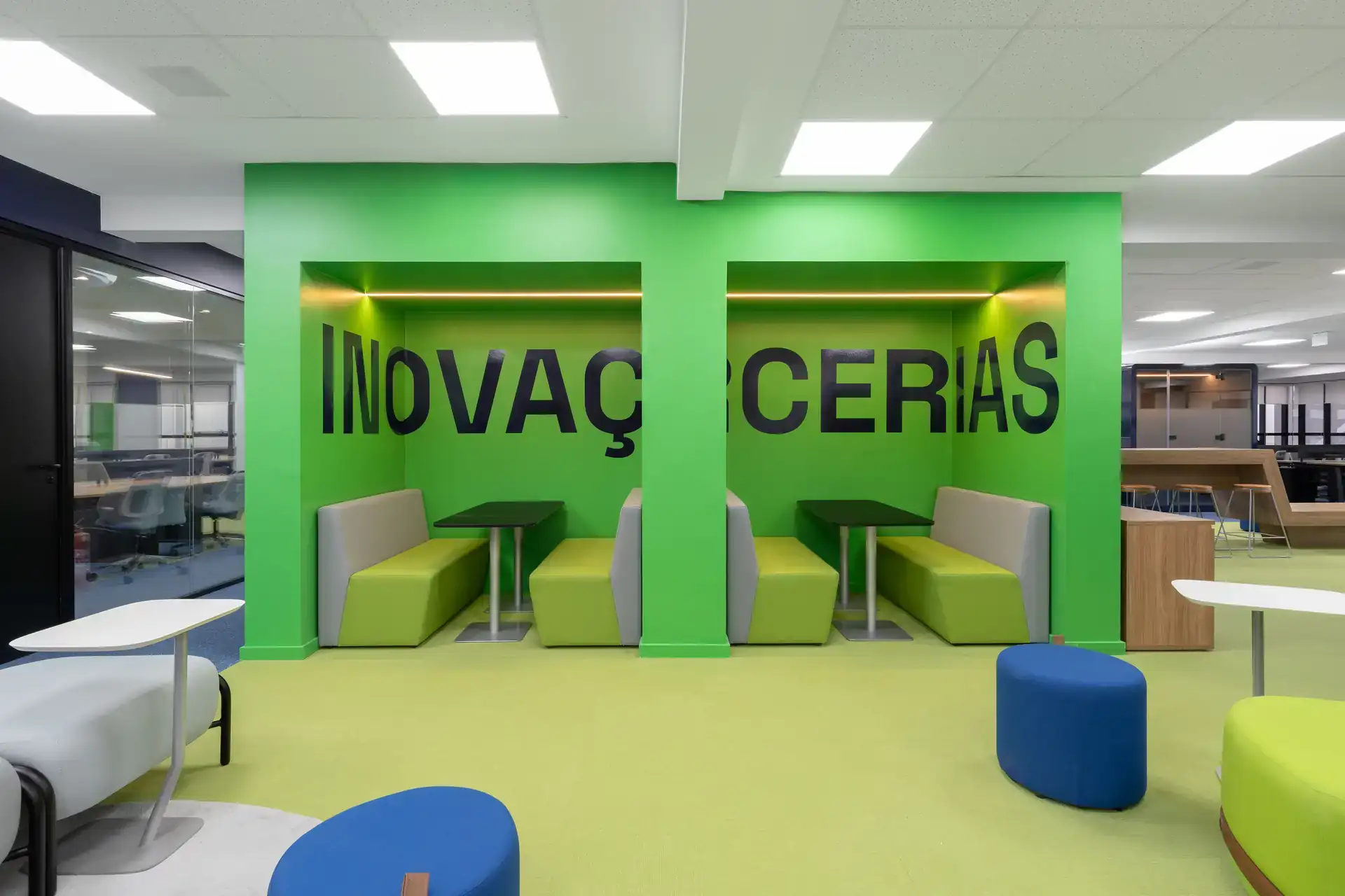 Área colaborativa com cabines verdes e mesas de apoio, criada em projeto de arquitetura corporativa para incentivar reuniões rápidas e inovação dentro do escritório.