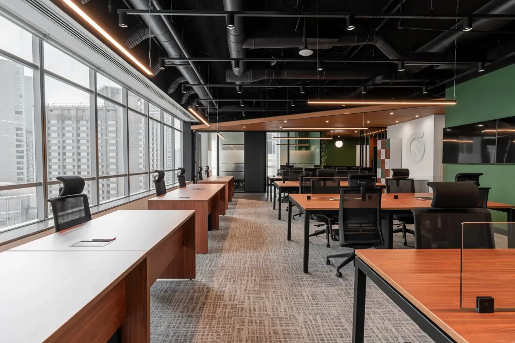 Vista ampla de estação de trabalho em obra corporativa do escritório da Oplium, com mesas em madeira, cadeiras ergonômicas e janelas panorâmicas, mostrando resultado de projeto de arquitetura funcional.