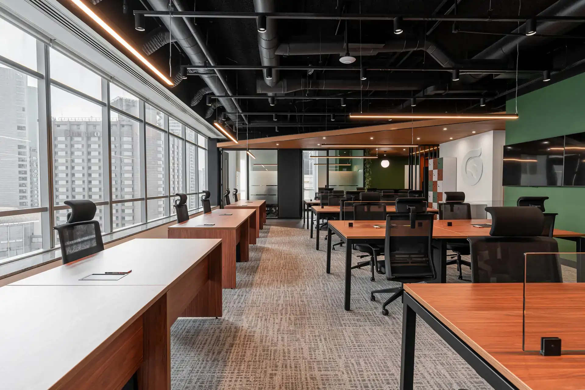 Vista ampla de estação de trabalho em obra corporativa do escritório da Oplium, com mesas em madeira, cadeiras ergonômicas e janelas panorâmicas, mostrando resultado de projeto de arquitetura funcional.