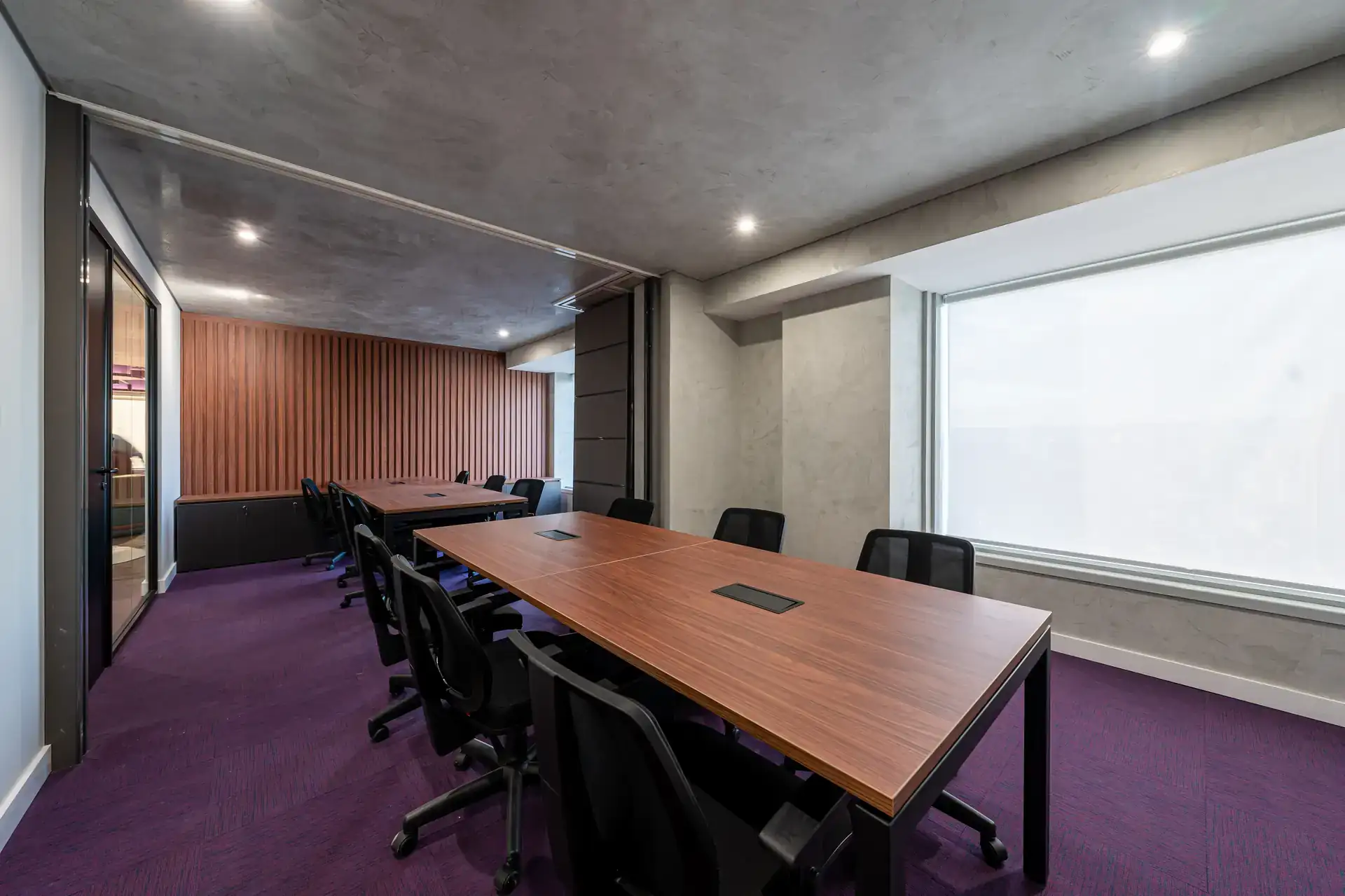 Ambiente corporativo finalizado do escritório da Inove com mesas em madeira, cadeiras pretas e carpete roxo. Projeto de arquitetura e obra corporativa concluída.