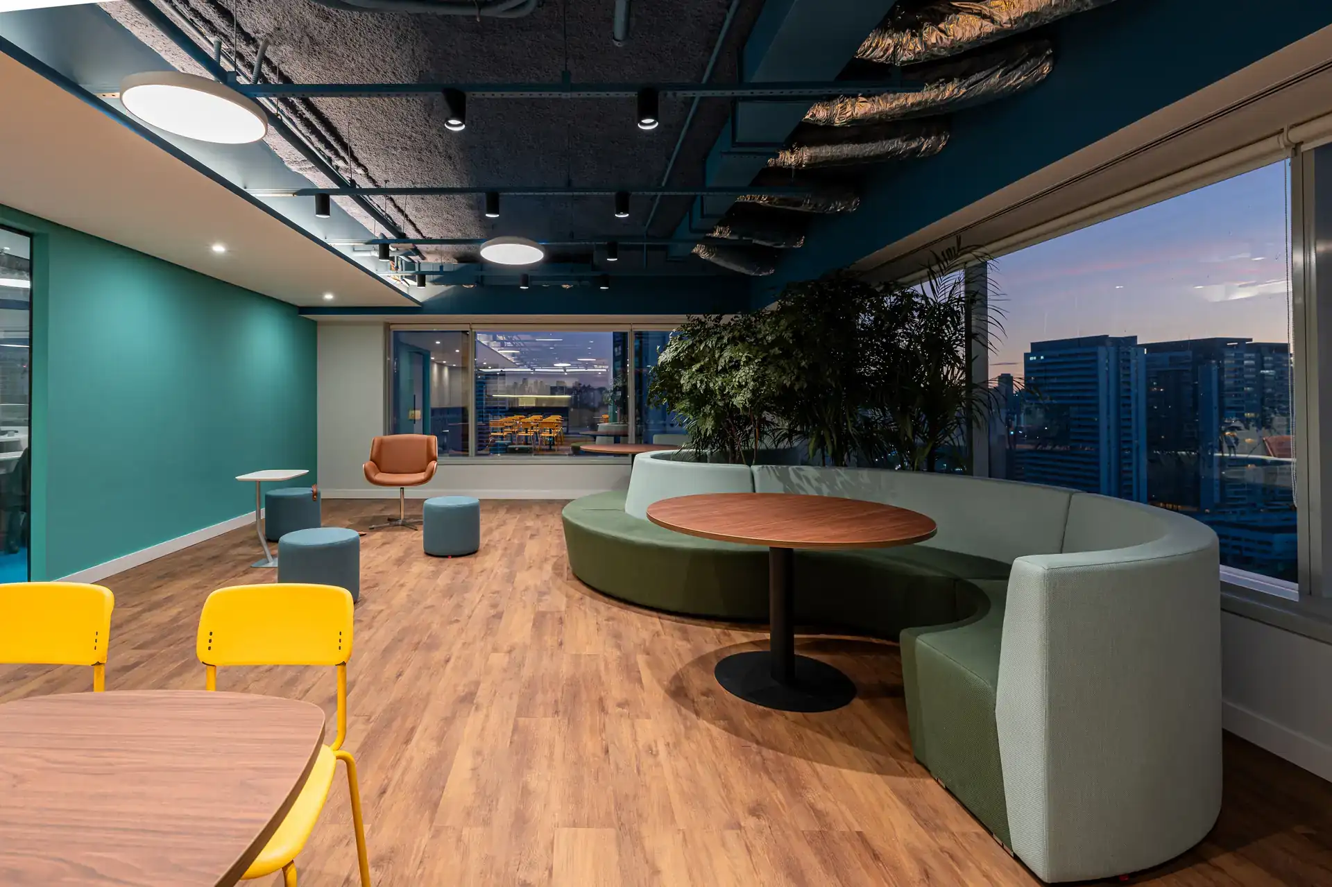 Área de convivência do escritório da Inove finalizada com sofás arredondados, mesas de apoio e vista da cidade. Reforma corporativa concluída com foco no bem-estar.