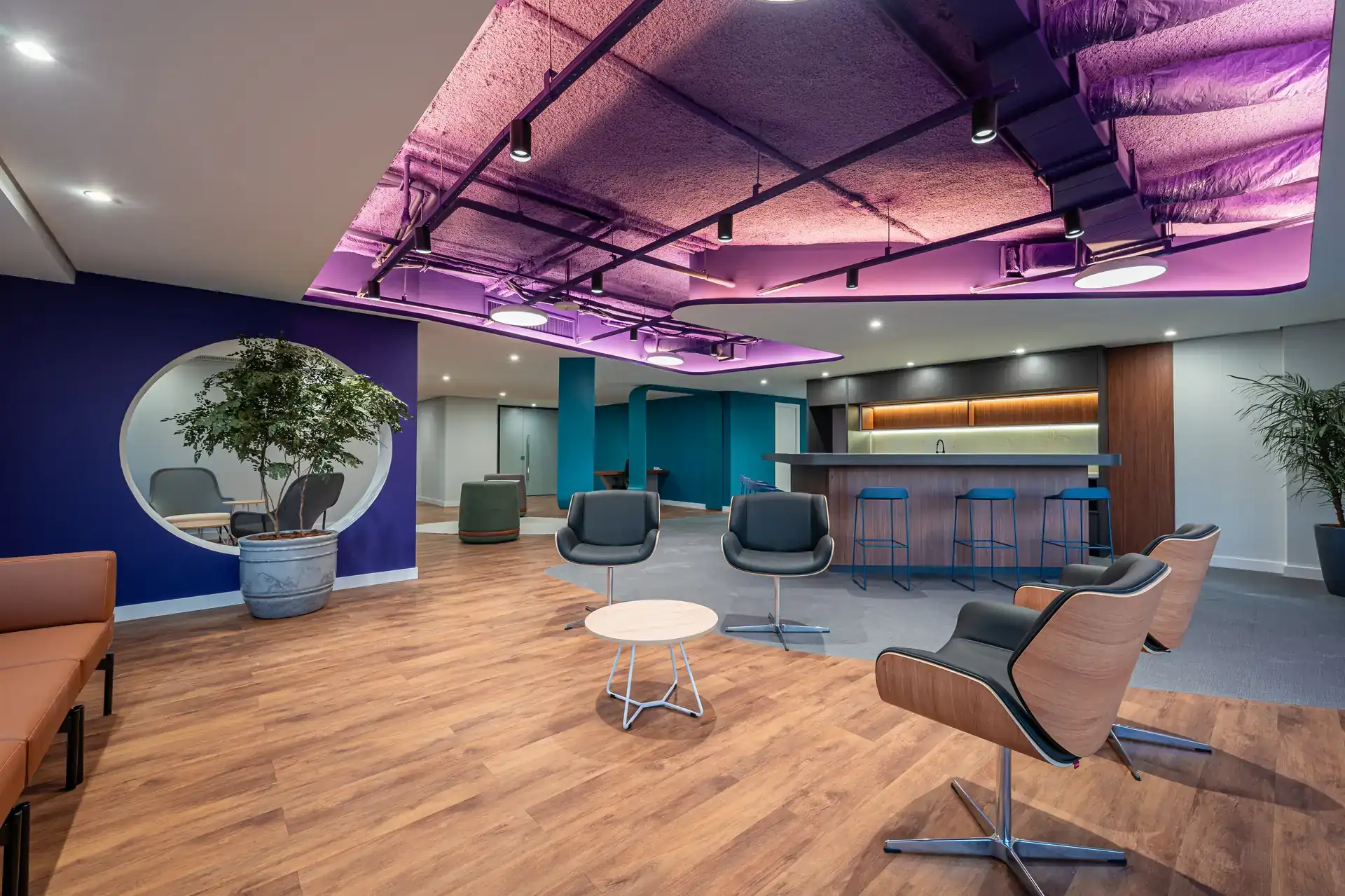 Área de descompressão do escritório da Inove finalizada com teto roxo iluminado, bar interno e mobiliário moderno. Projeto de arquitetura e reforma corporativa concluída.