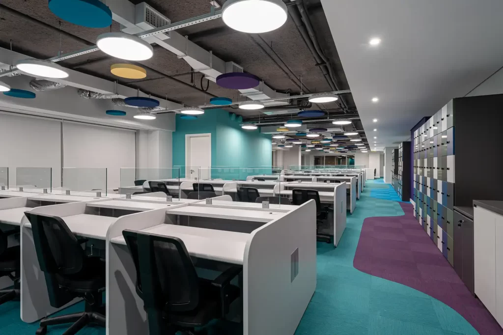 Área ampla tipo call center do escritório da Inove, parte do projeto de arquitetura  corporativa e obra corporativa concluída, com mesas brancas, cadeiras pretas e forro industrial.