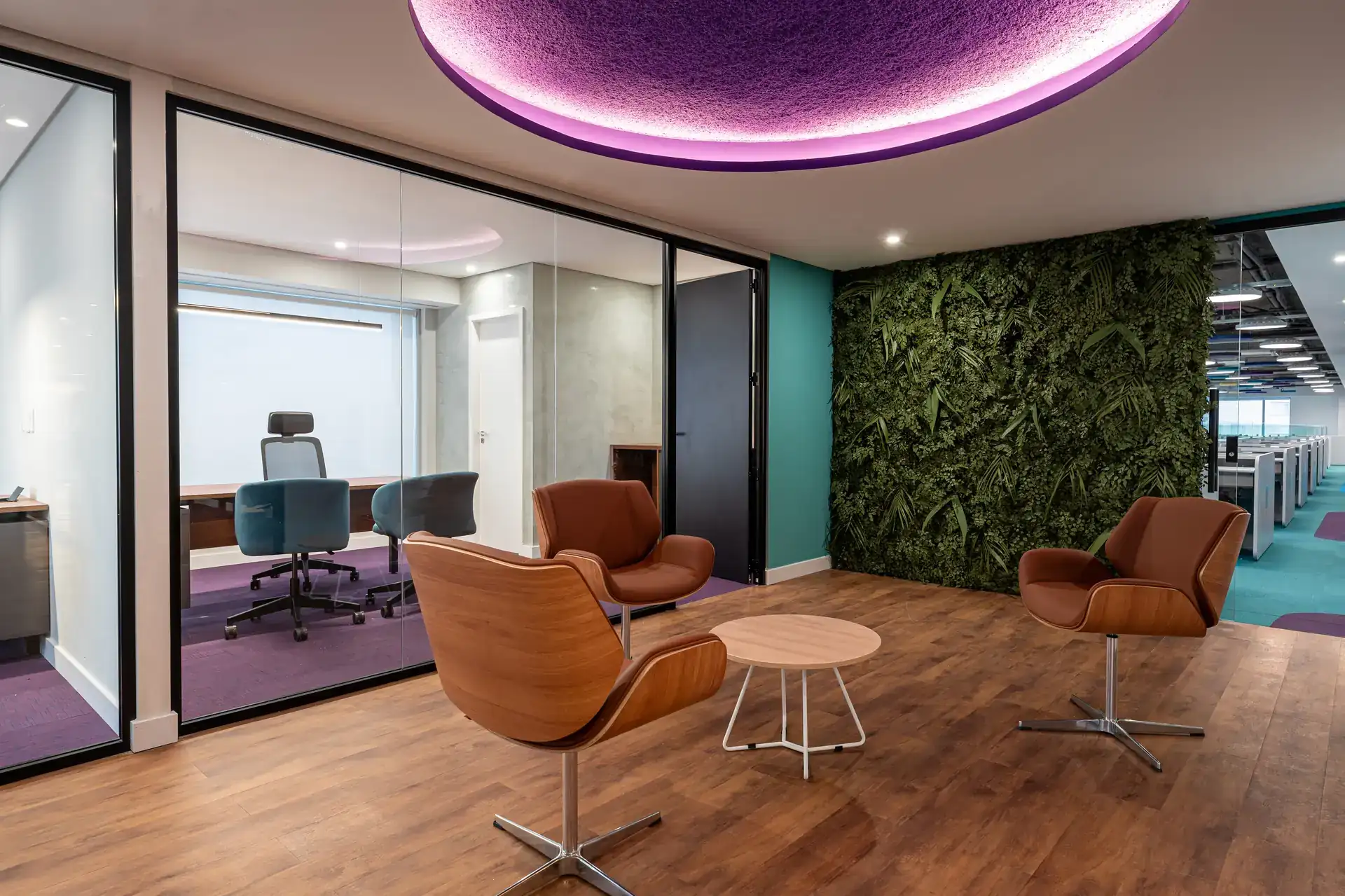 Lounge finalizado do escritório da Inove com poltronas caramelo, iluminação roxa e parede verde. Projeto de arquitetura focado em bem-estar corporativo.