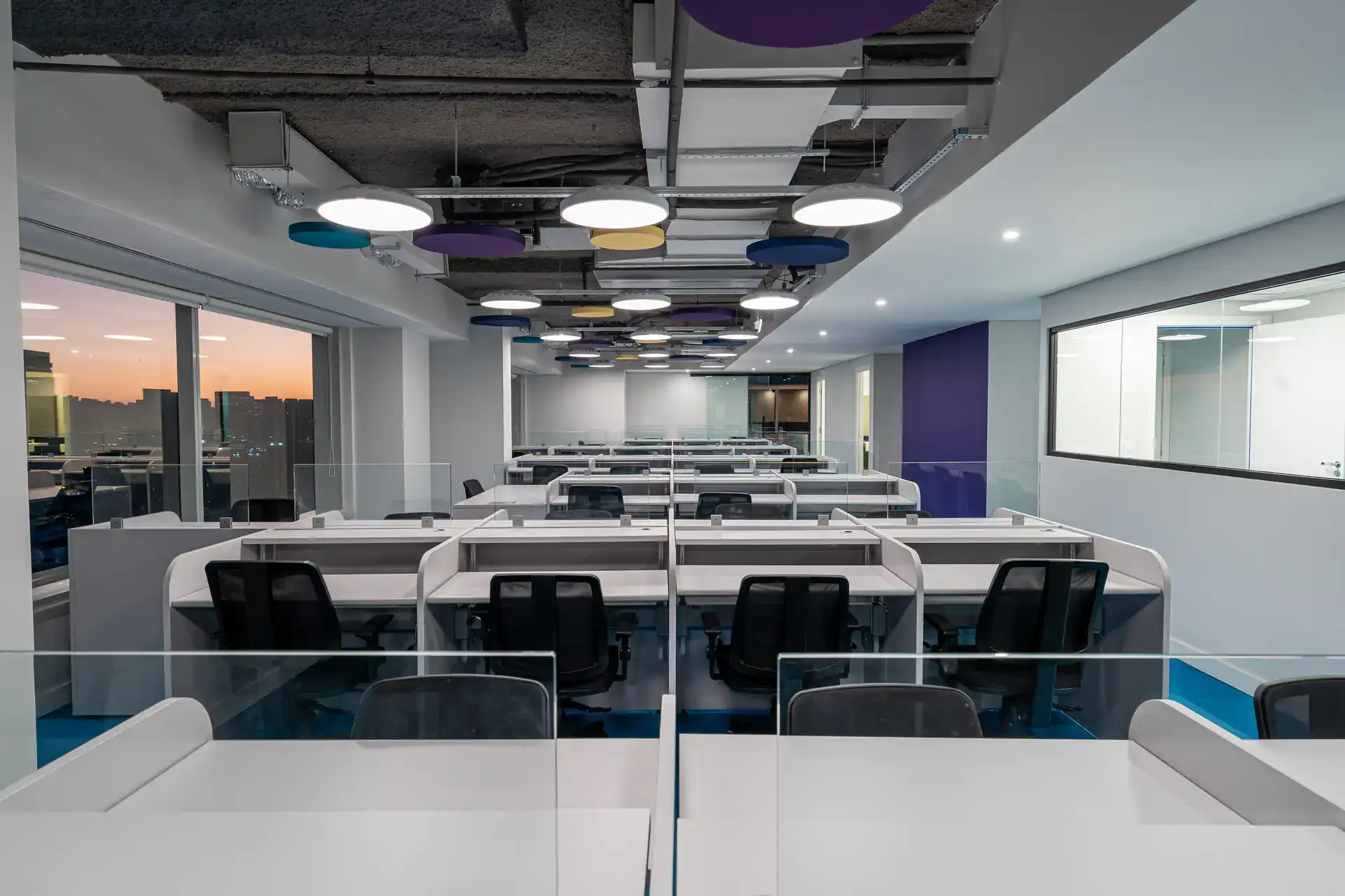 Estações de trabalho no open floor do escritório da Inove, obra corporativa finalizada, com mesas modulares, divisórias de vidro e forro técnico com painéis circulares.