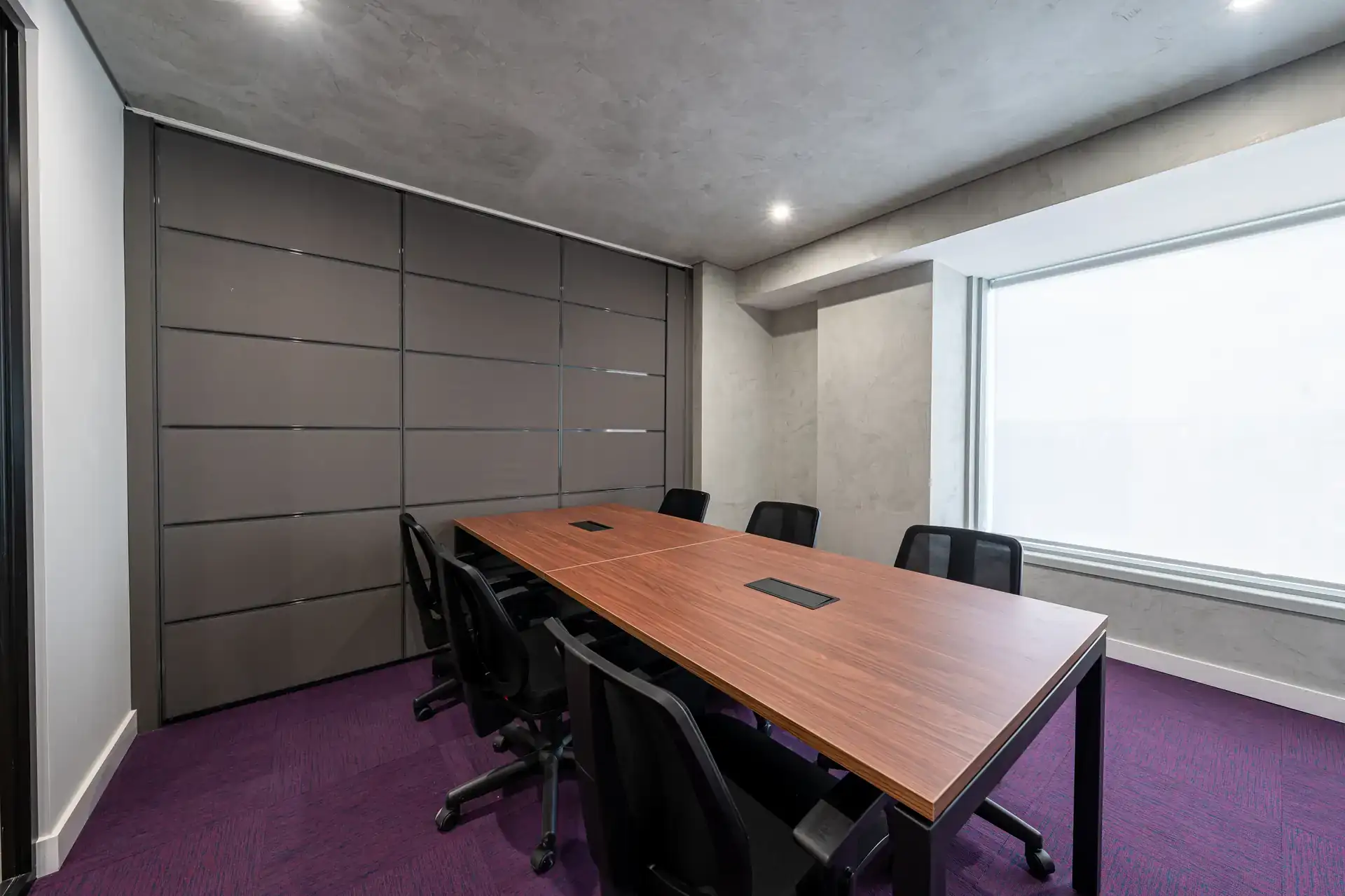 Sala de reunião finalizada do escritório da Inove com mesa em madeira, cadeiras pretas e carpete roxo. Projeto de arquitetura e reforma corporativa com acabamento premium.