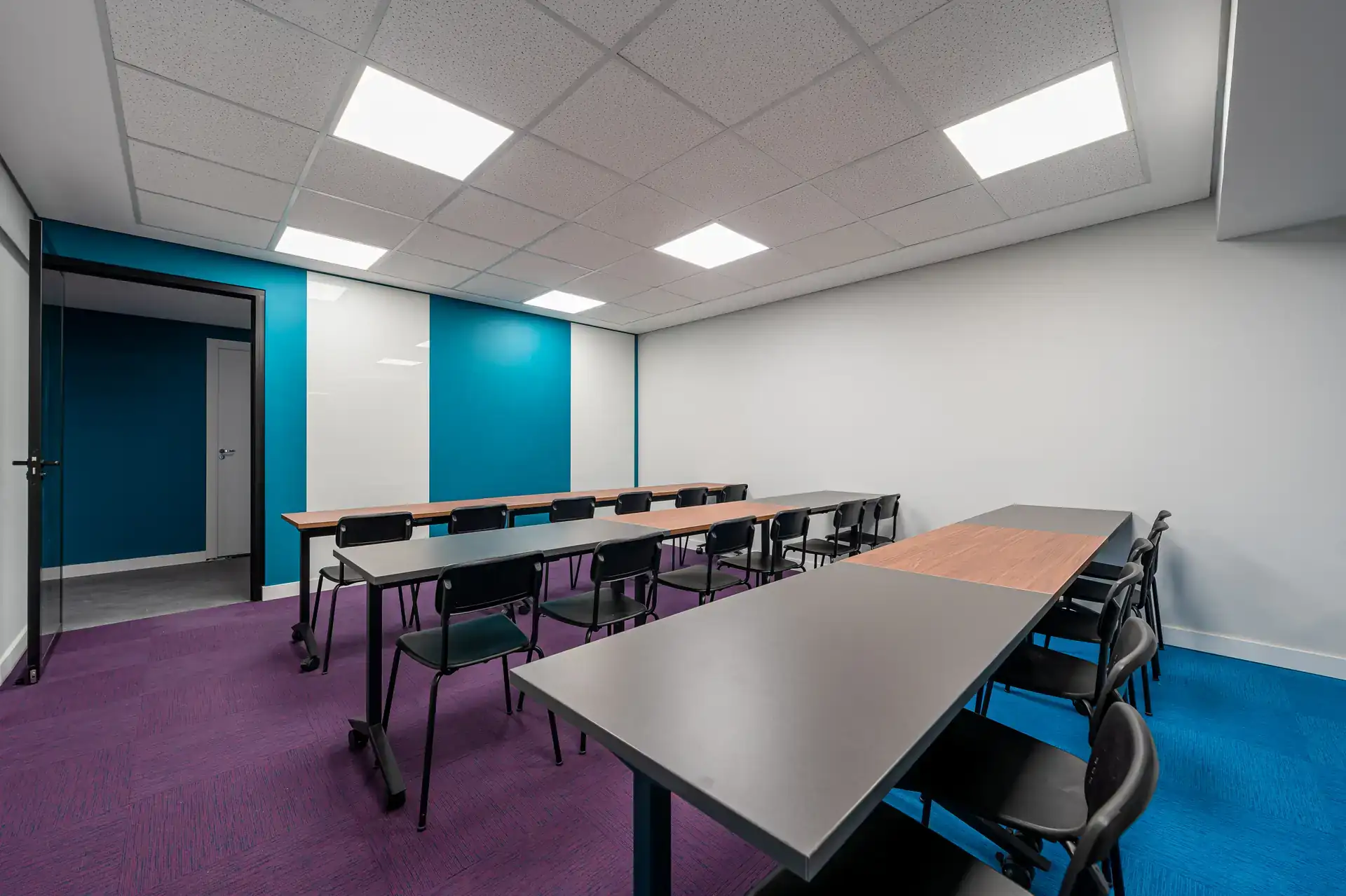 Sala de treinamento finalizada do escritório da Inove com mesas duplas, cadeiras pretas e paredes azul e branco. Reforma corporativa e projeto de arquitetura concluídos.