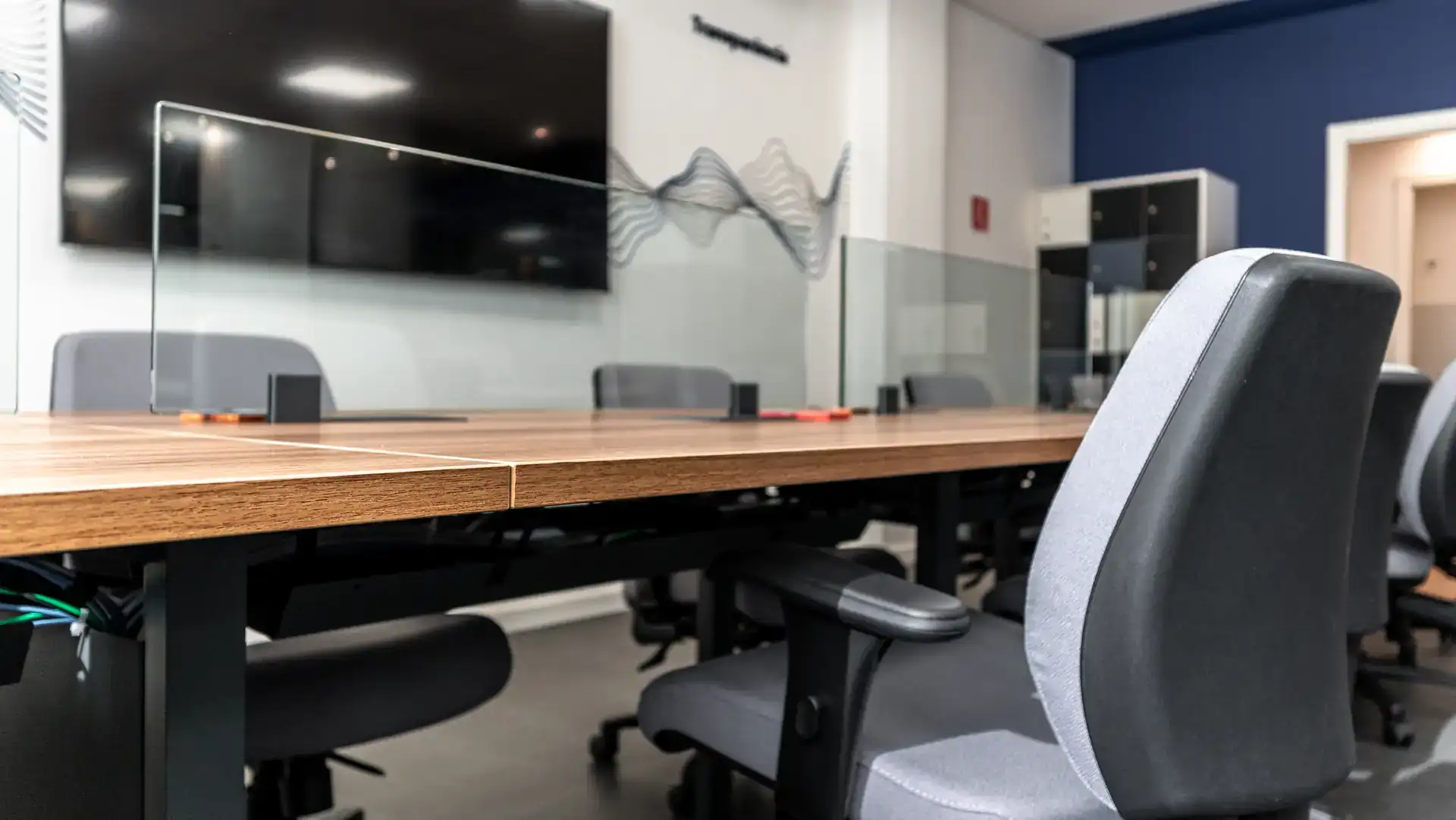 Detalhe de mesa corporativa em madeira com divisória de vidro e cadeiras cinza, evidenciando o cuidado do escritório de arquitetura com ergonomia e acabamento.