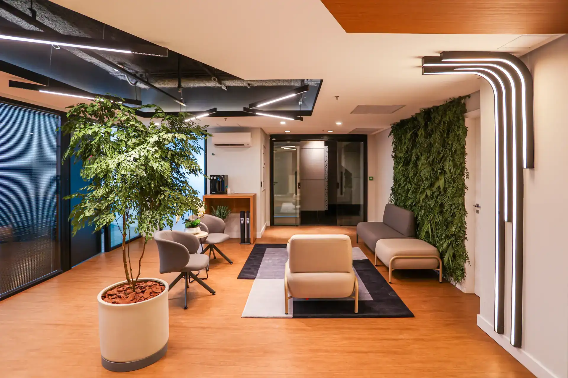 Lounge moderno da Andra com parede verde, sofás e iluminação linear, evidenciando projeto de arquitetura e reforma de escritório concluída em obra corporativa eficiente.