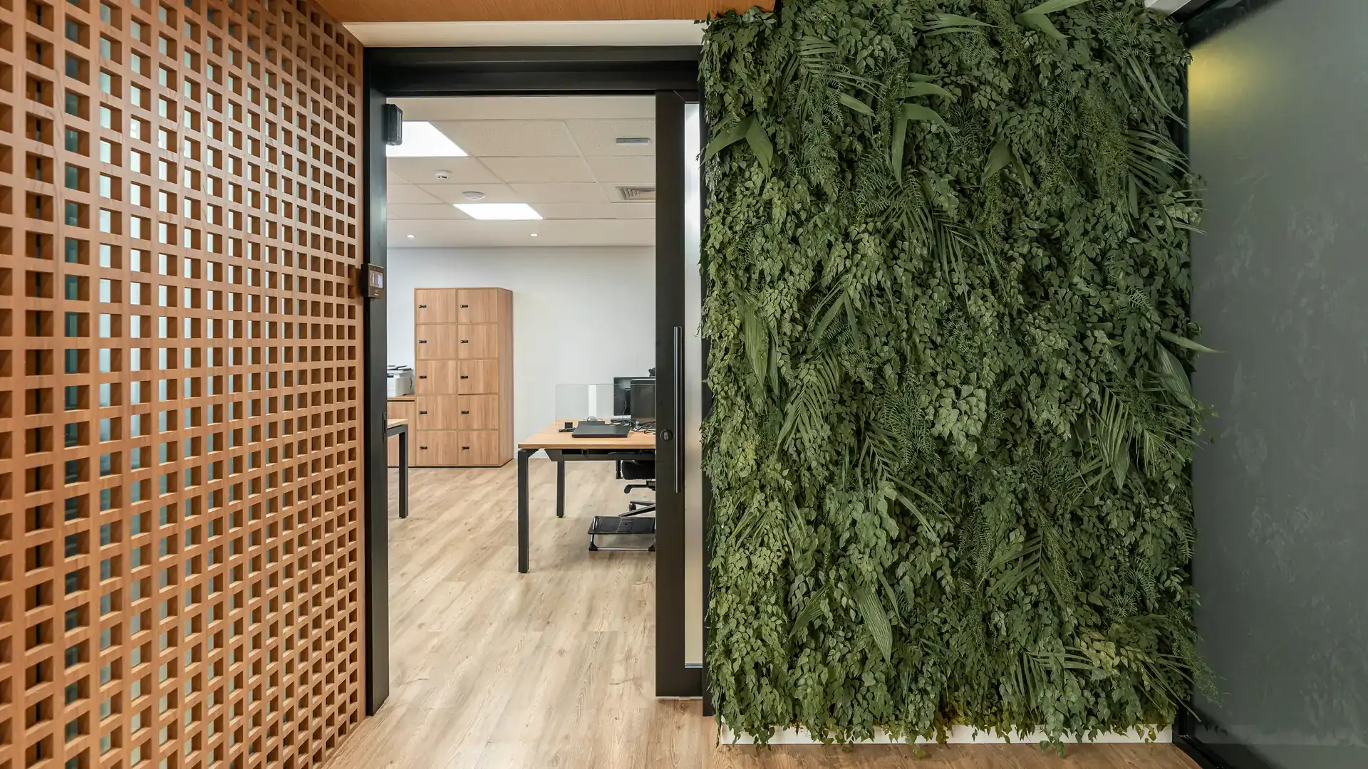 Acesso ao escritório com parede verde natural e painel ripado em madeira, elementos presentes na obra corporativa da MHM.