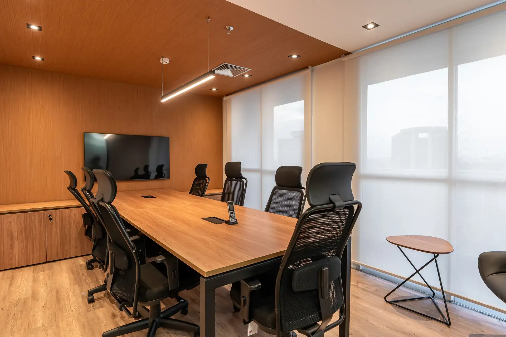 Sala de diretoria com mesa de madeira, cadeiras ergonômicas e iluminação linear, desenvolvida no projeto de arquitetura corporativa do escritório da MHM.