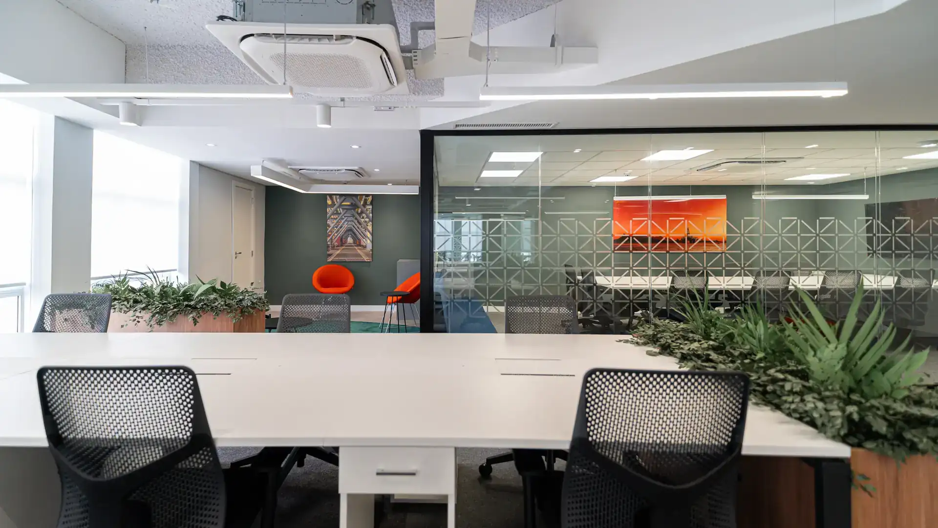 Open space com mesas compartilhadas, plantas centrais e grandes janelas, reforçando bem-estar no ambiente de trabalho corporativo, no escritório da NSG após reforma completa com projeto de arquitetura corporativa e obra corporativa.