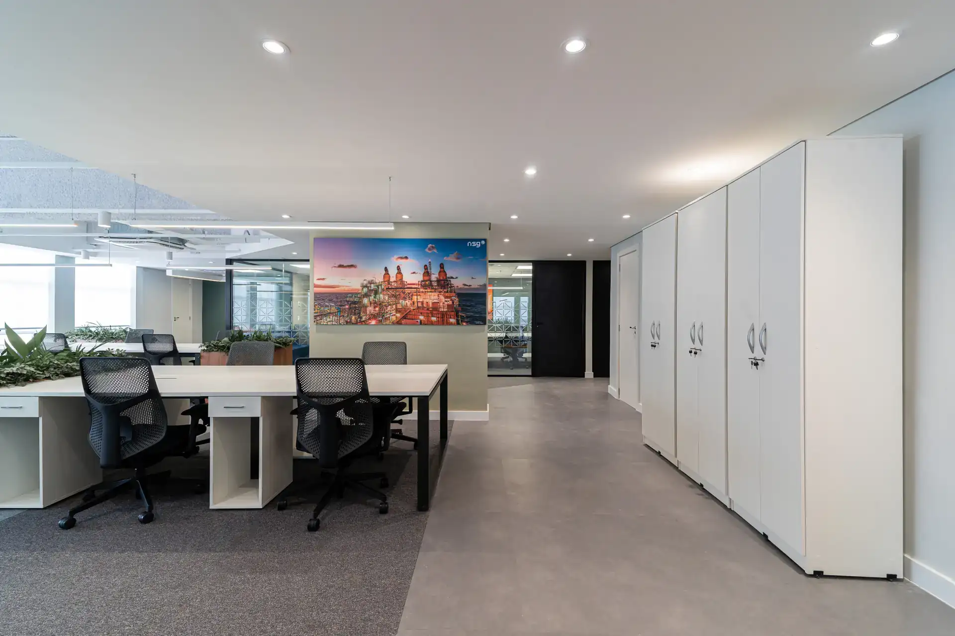 Ambiente open space do escritório da NSG, após reforma corporativa com projeto de arquitetura e obra, com mesas em linha, vegetação integrada e armários brancos, ideal para equipes em escritórios modernos.