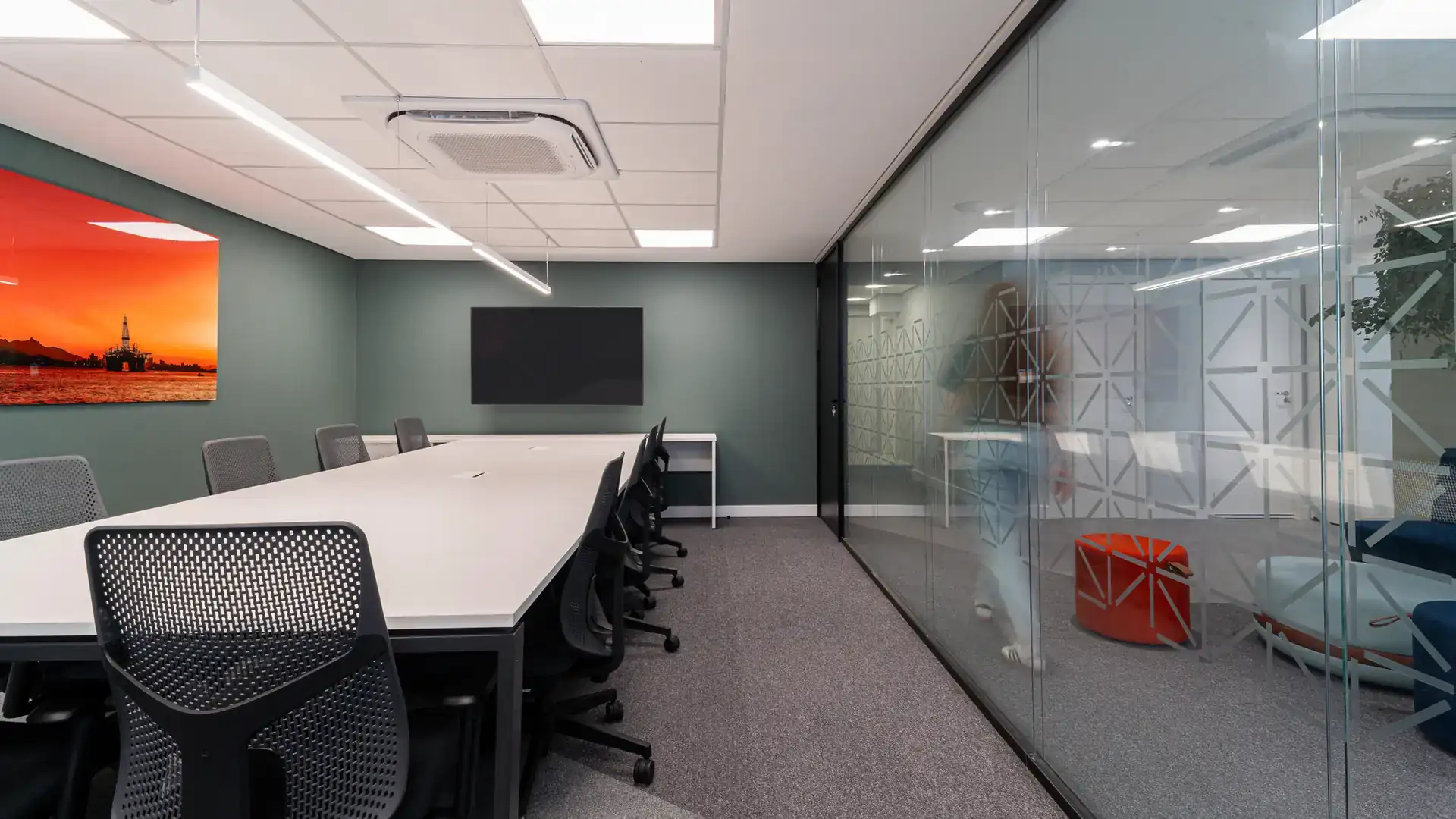 Sala de reunião com divisórias de vidro e obra decorativa laranja, integrando estética e funcionalidade no escritório da NSG, após uma reforma coporativa completa com projeto de arquitetura e obra rápida.