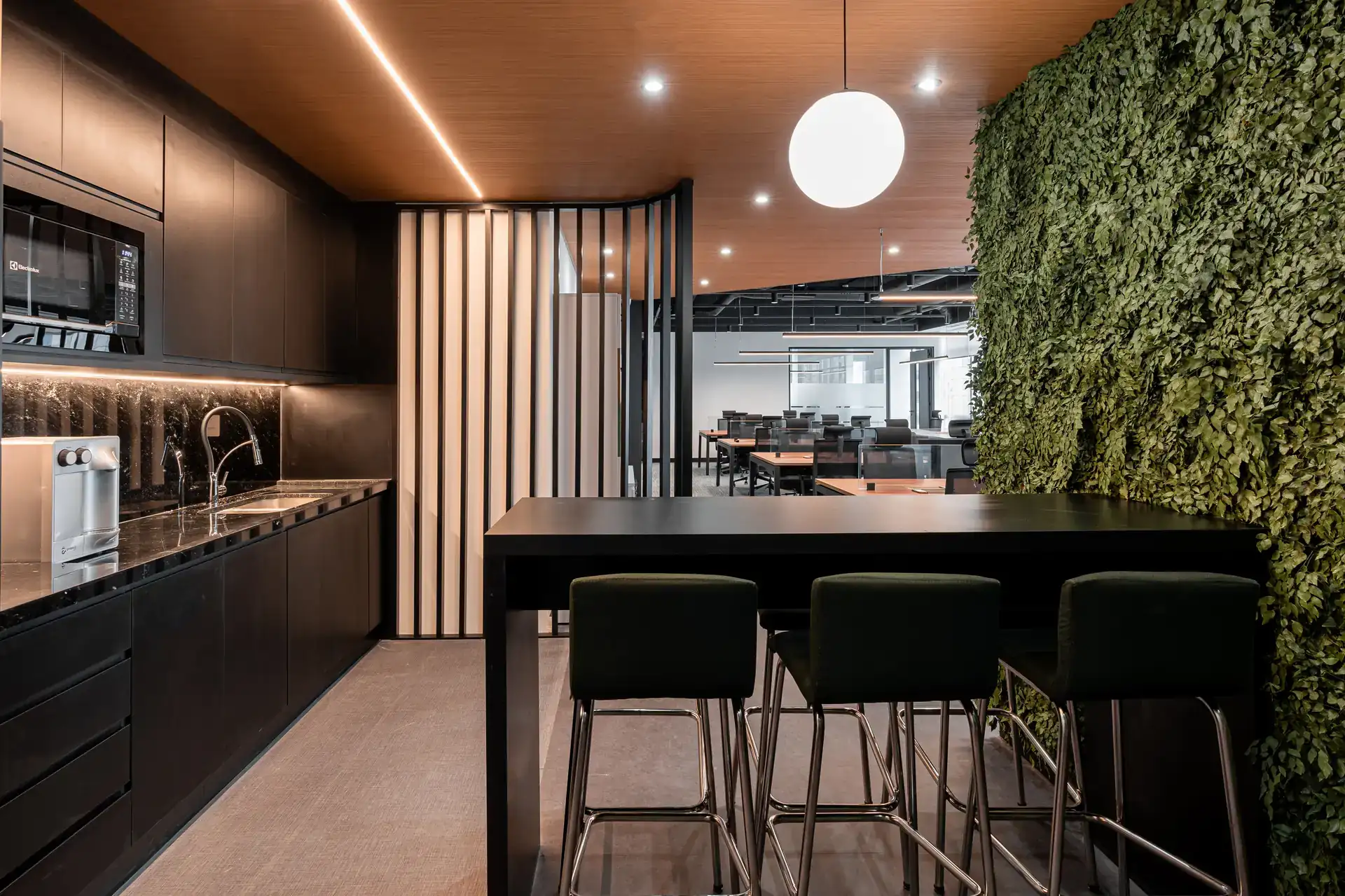 Copa gourmet do escritório da Oplium com armários pretos, bancada em pedra e muro verde, integrando design corporativo e funcionalidade, pensados em projetos de arquitetura e obra corporativa.