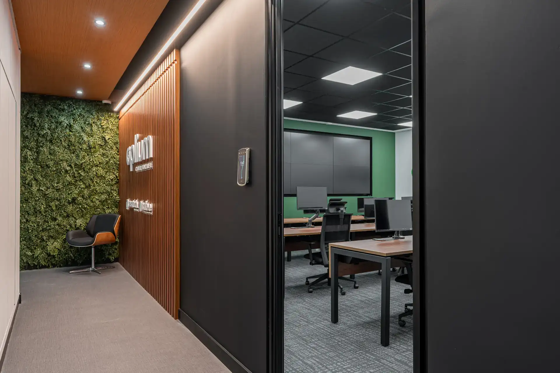 Hall de entrada do escritório da Oplium com parede verde e painel ripado iluminado, integrando área de circulação ao ambiente técnico em uma obra corporativa contemporânea, com projeto de arquitetura integrado.