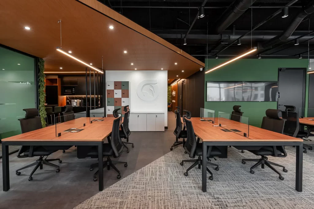 Ambiente open office do escritório da Oplium com mesas colaborativas, lockers coloridos e elementos de madeira, destacando o projeto de arquitetura e obra corporativa do escritório.