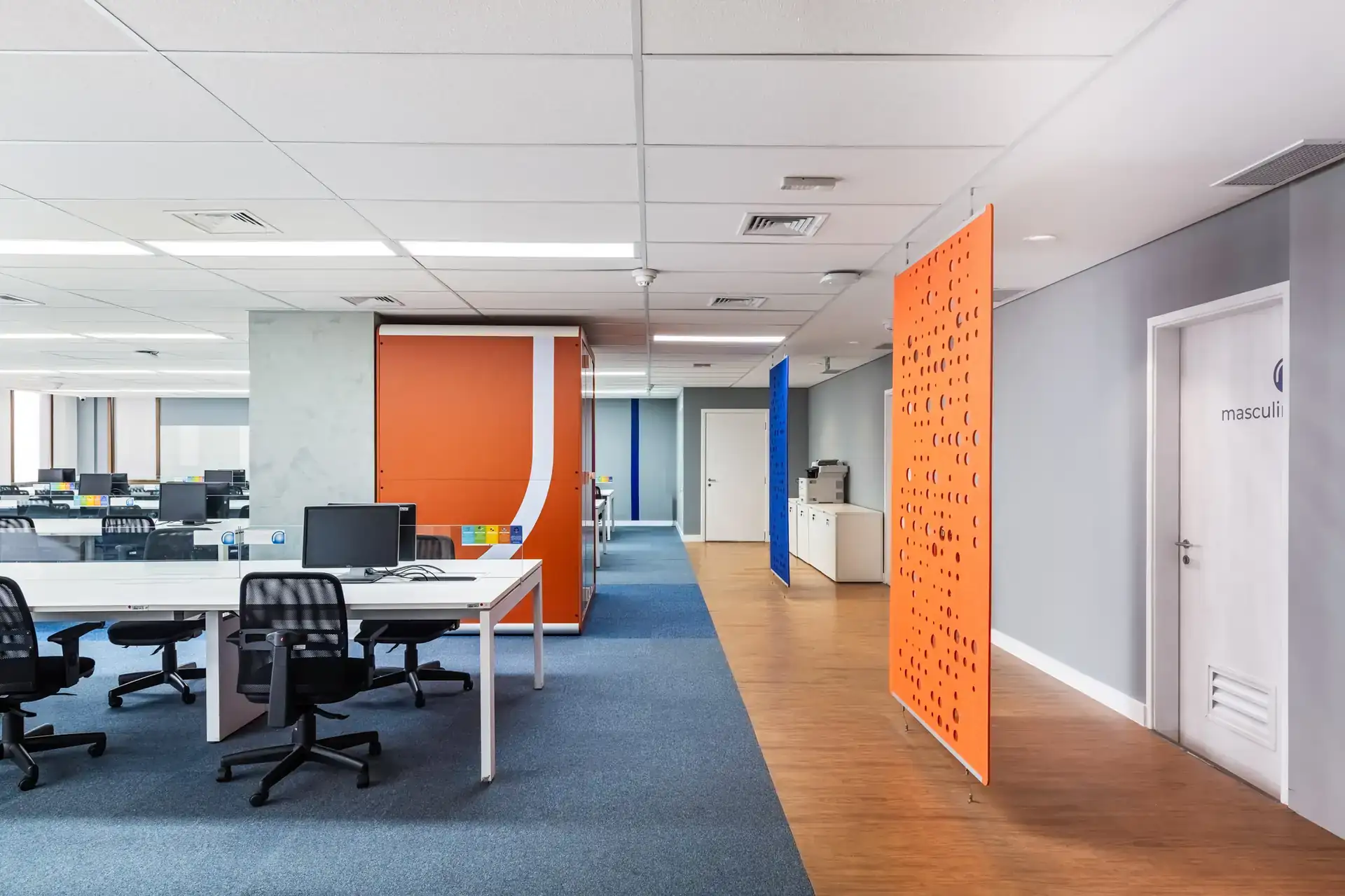 Corredor corporativo com phonebooth laranja e áreas de trabalho abertas, destacando soluções de arquitetura funcional. Resultado de uma reforma corporativa com projeto de arquitetura e obra para o escritório da Recovery.