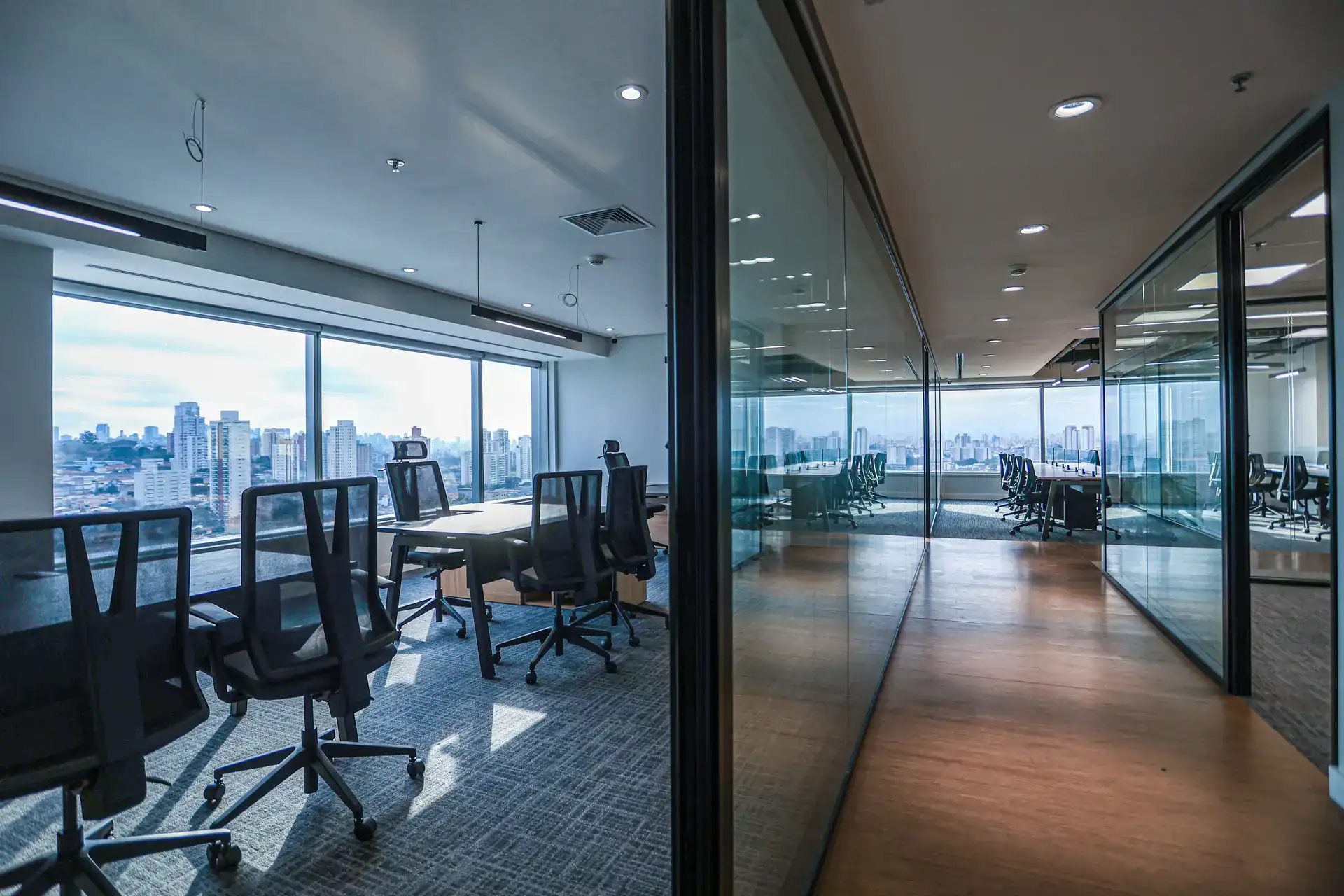 Sala corporativa envidraçada com vista para a cidade, estações de trabalho e iluminação moderna, mostrando projeto de arquitetura e obra corporativa finalizada após reforma de escritório.