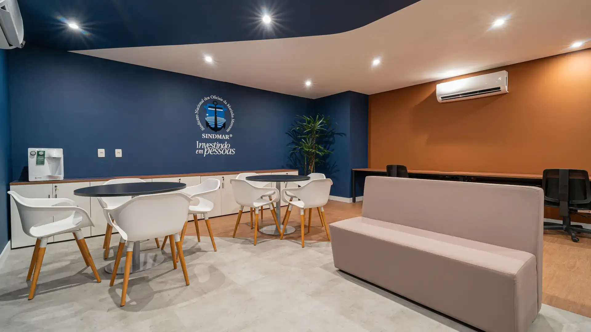 Área colaborativa com mesas brancas e cadeiras modernas, planejada dentro do projeto de arquitetura e obra corporativa do escritório do SINDMAR.