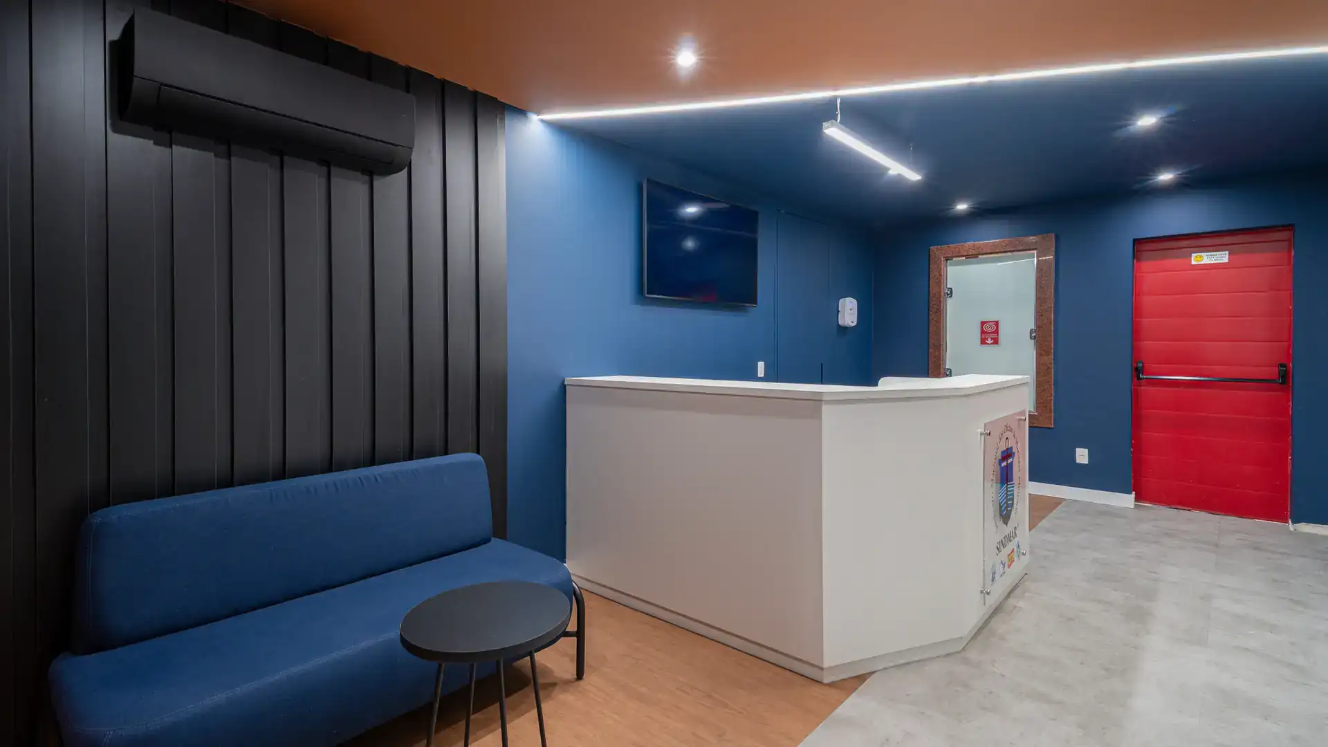 Recepção com sofá azul e painel preto vertical, ambiente renovado na reforma de escritório do SINDMAR, com projeto de arquitetura corporativa e obra.