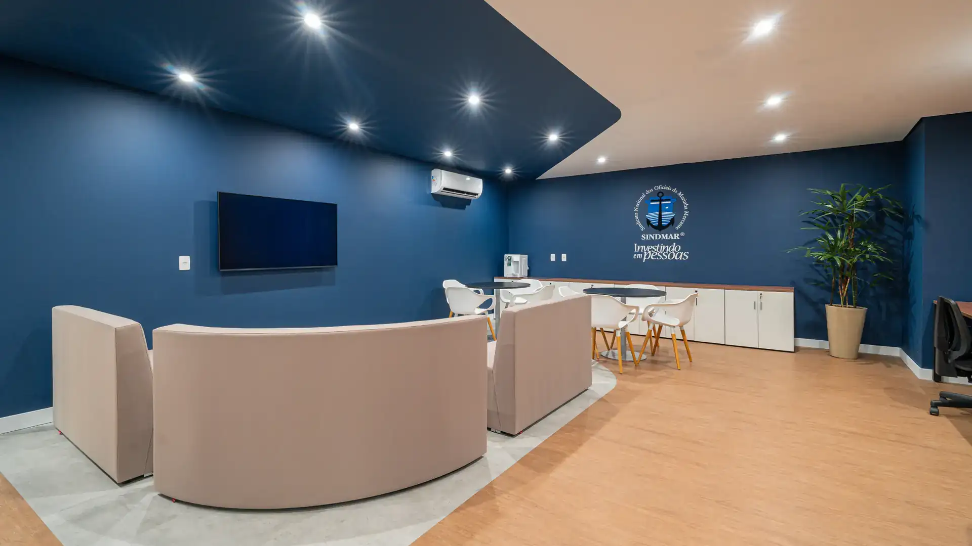 Ambiente de convivência com TV, sofás curvos e parede azul, parte da reforma de escritório realizada no SINDMAR, pelo escritório de arquitetura corporativa, Custódio.