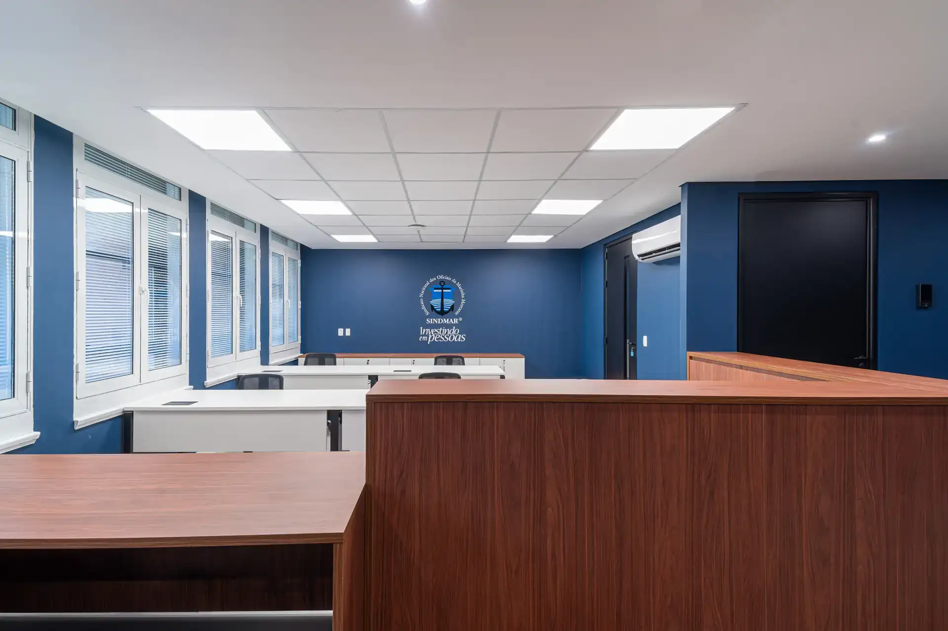 Sala operacional do SINDMAR com estações alinhadas e parede azul institucional, parte de um projeto de arquitetura e reforma corporativa.