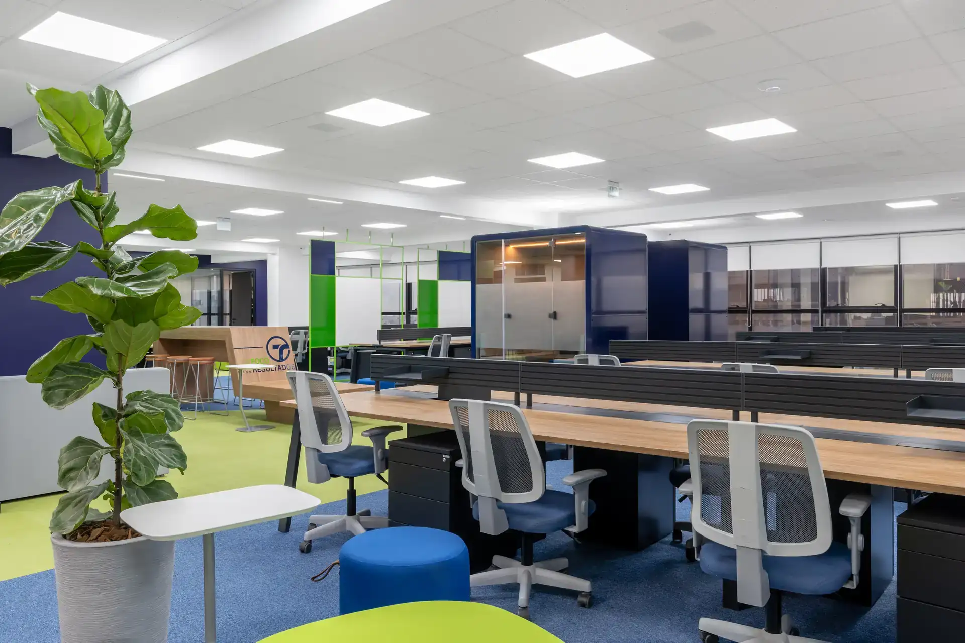 Open space corporativo com estações de trabalho, phone booth envidraçada e áreas colaborativas, destacando soluções de projeto de arquitetura e reforma de escritório da Transit BR.