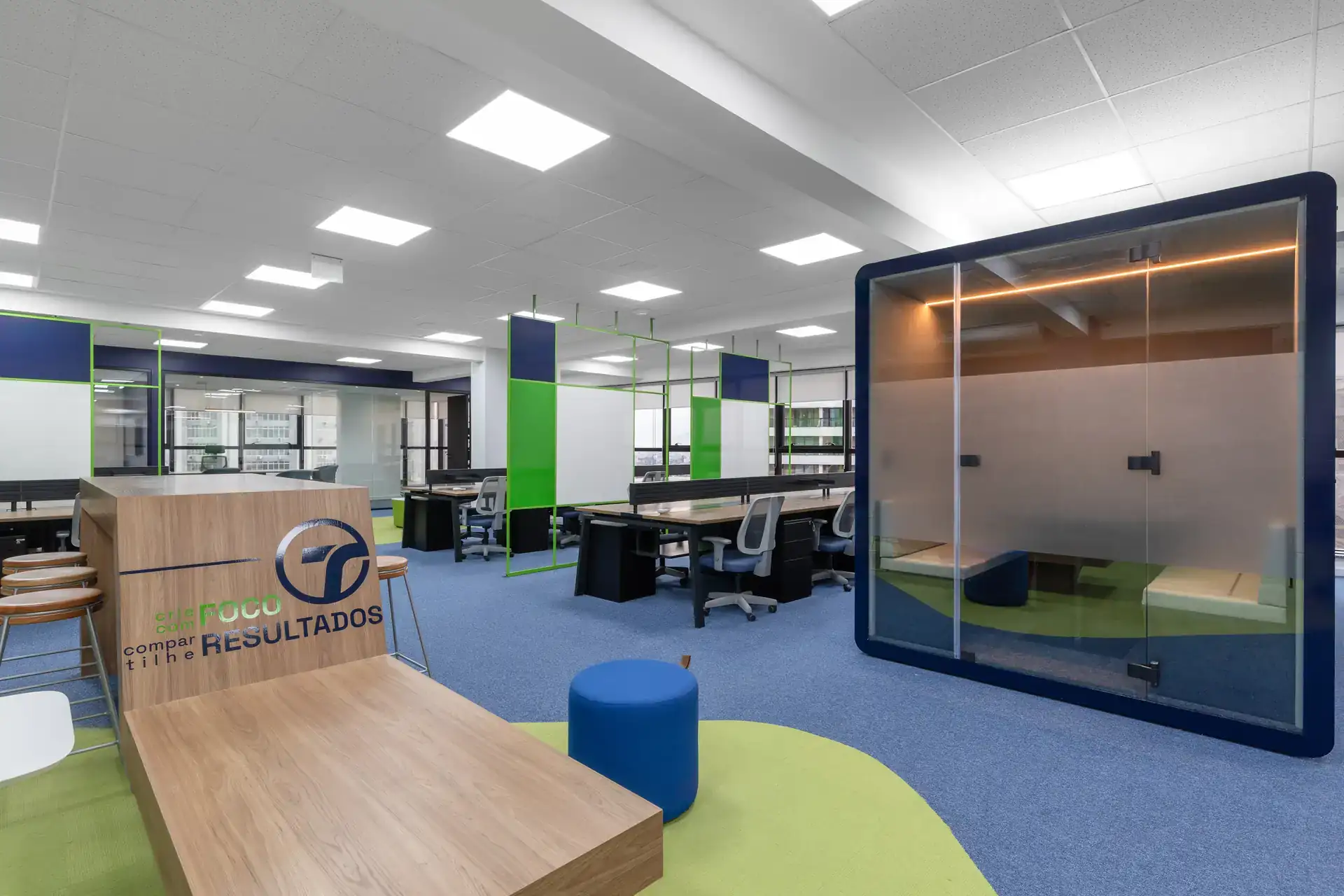 Open office moderno com mesa de colaboração, phone booth envidraçada e estações de trabalho projetadas por escritório de arquitetura especializado em reforma de escritório corporativa.