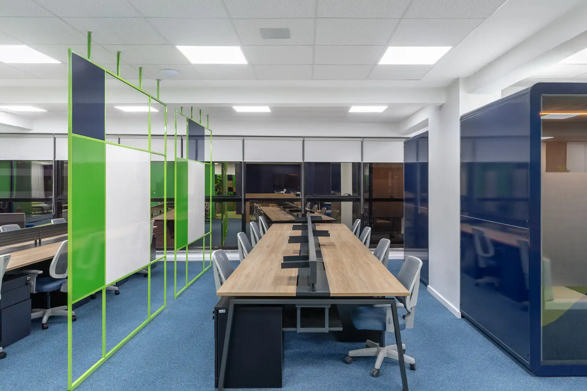 Estações de trabalho compartilhadas com divisórias verdes e phonebooths ao fundo, mostrando solução de projeto de arquitetura para open space na obra corporativa da Transit BR.
